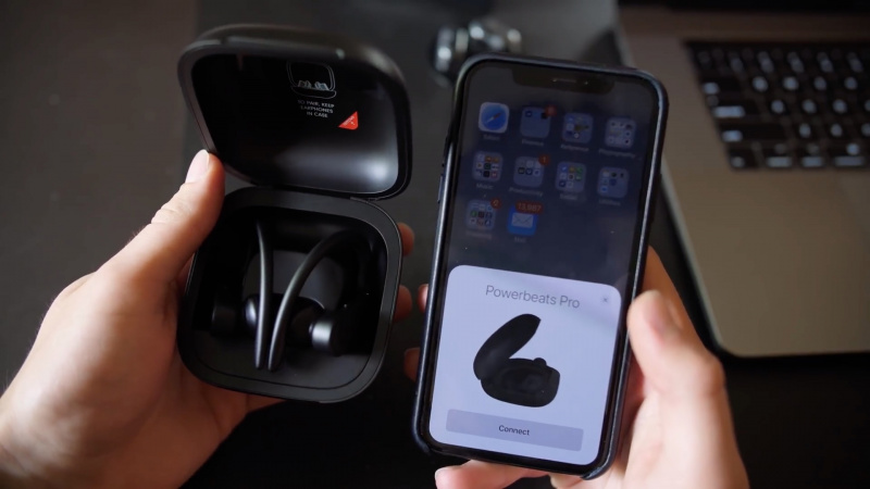  Мъжка ръка, която държи Powerbeats Pro в калъфа им за зареждане до iPhone.